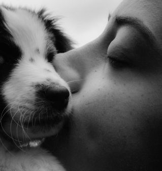 A black and white photo of a woman kissing a dog